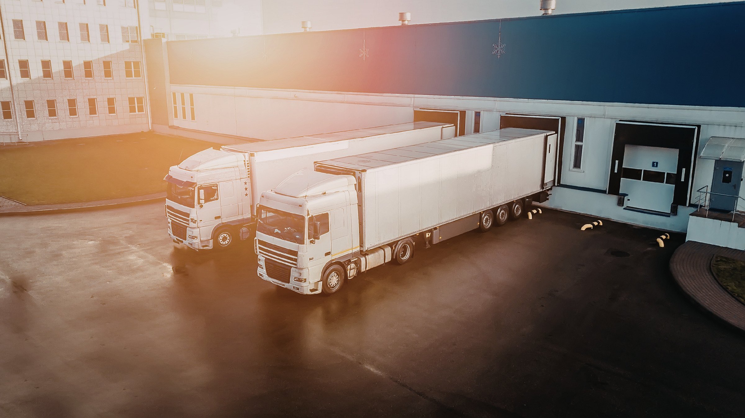 3PL warehouse loading bay with two semi-trailer trucks reversing into dock doors for freight distribution at a logistics facility.